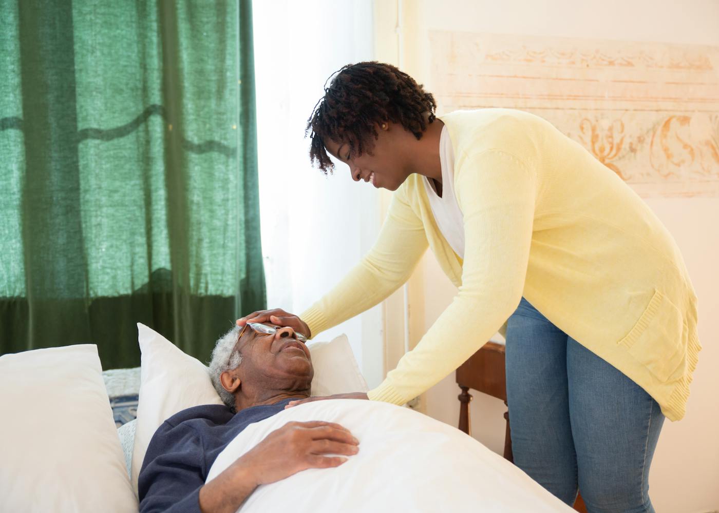 A caregiver tending warmly to an elderly man resting at home